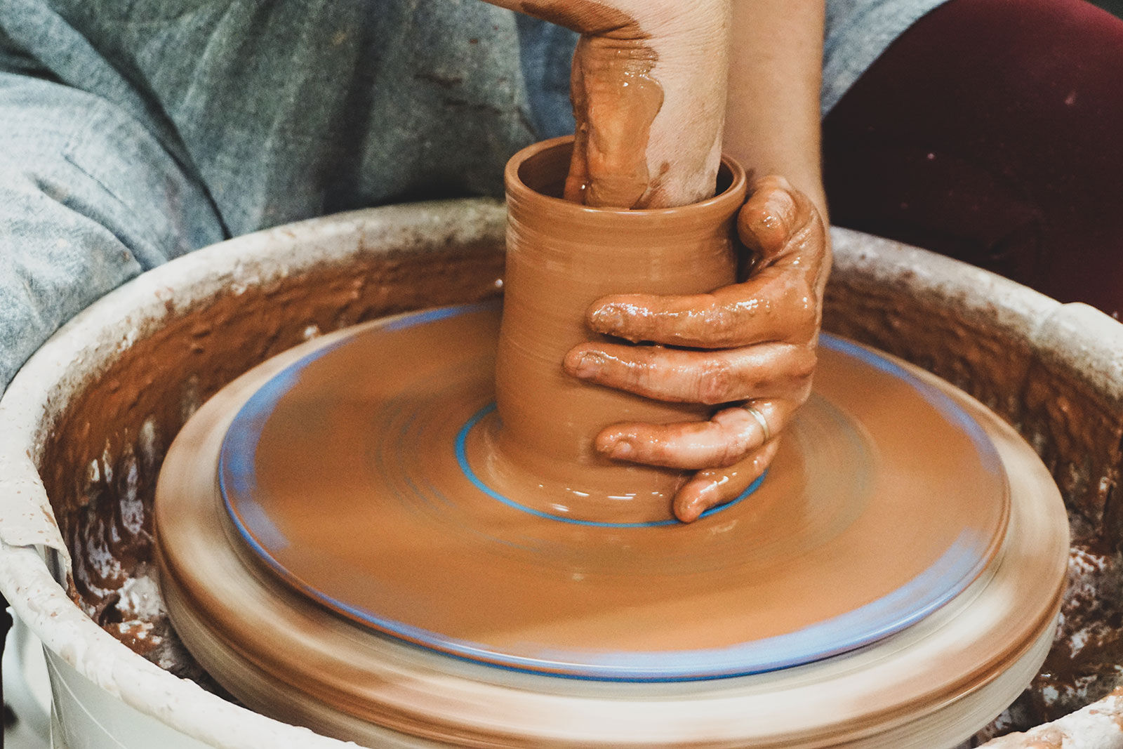 A hand forming a clay vessel on a pottery wheel
